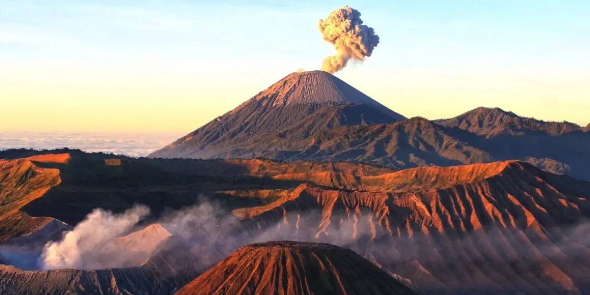 Volcanos at sunrise: one large one in the background with a plume of smoke rising from it. Bromo, Indonesia